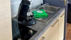 A modern kitchen with wooden cabinets, a built-in microwave, a coffee maker, and a stainless steel sink. - La Résidence Le Grand Tétras (Ax-les-Thermes)