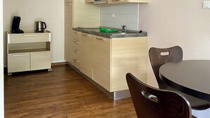 A compact kitchen with wooden cabinets, a microwave, and a coffee maker on a shelf. There is a dining table with chairs and a small cabinet with drawers. - La Résidence Le Grand Tétras (Ax-les-Thermes)
