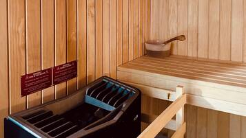 A sauna room with wooden walls, a bench, and a black heater. There are warning signs on the wall.