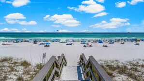 Ein Strand mit einer Holzpromenade, die zum Ufer führt, Sonnenschirmen und entspannten Personen.