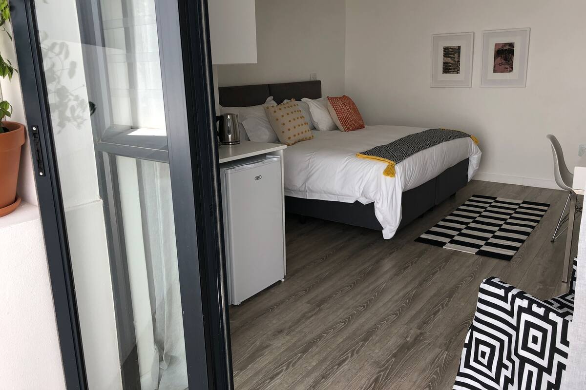 A bedroom with a bed, a small fridge, a desk, and a chair.