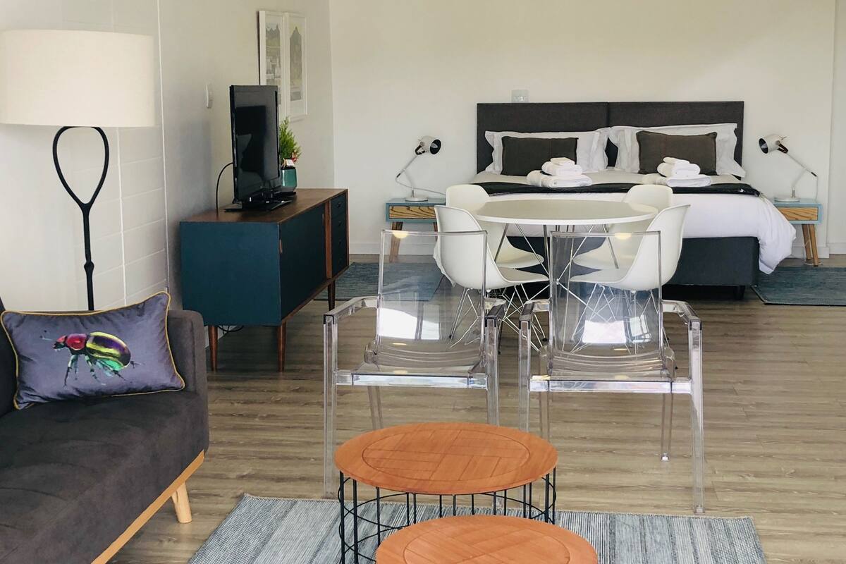 A modern hotel room with a bed, a TV, a desk, and a dining area.