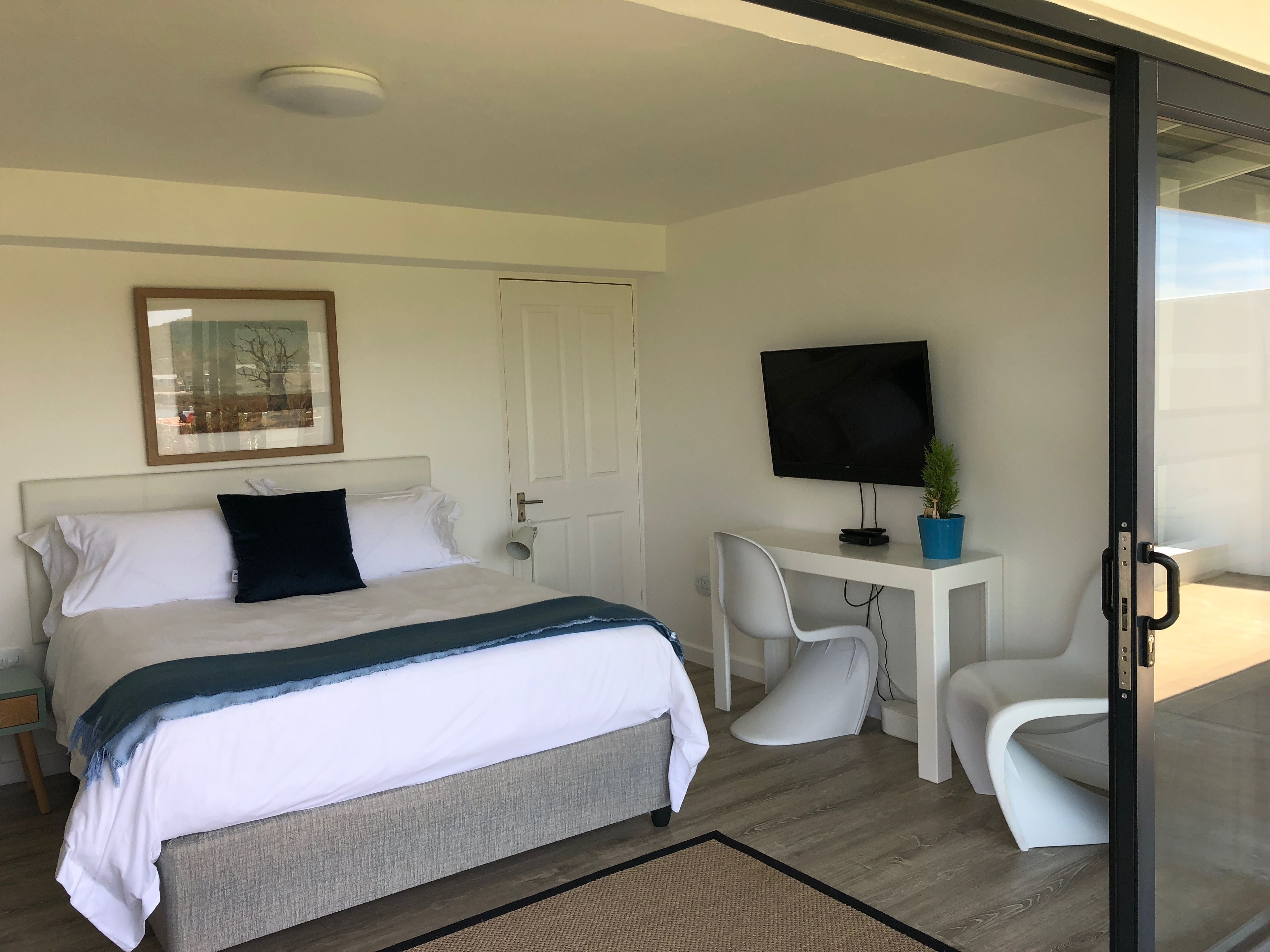A modern hotel room with a bed, a desk with a TV, and a chair.