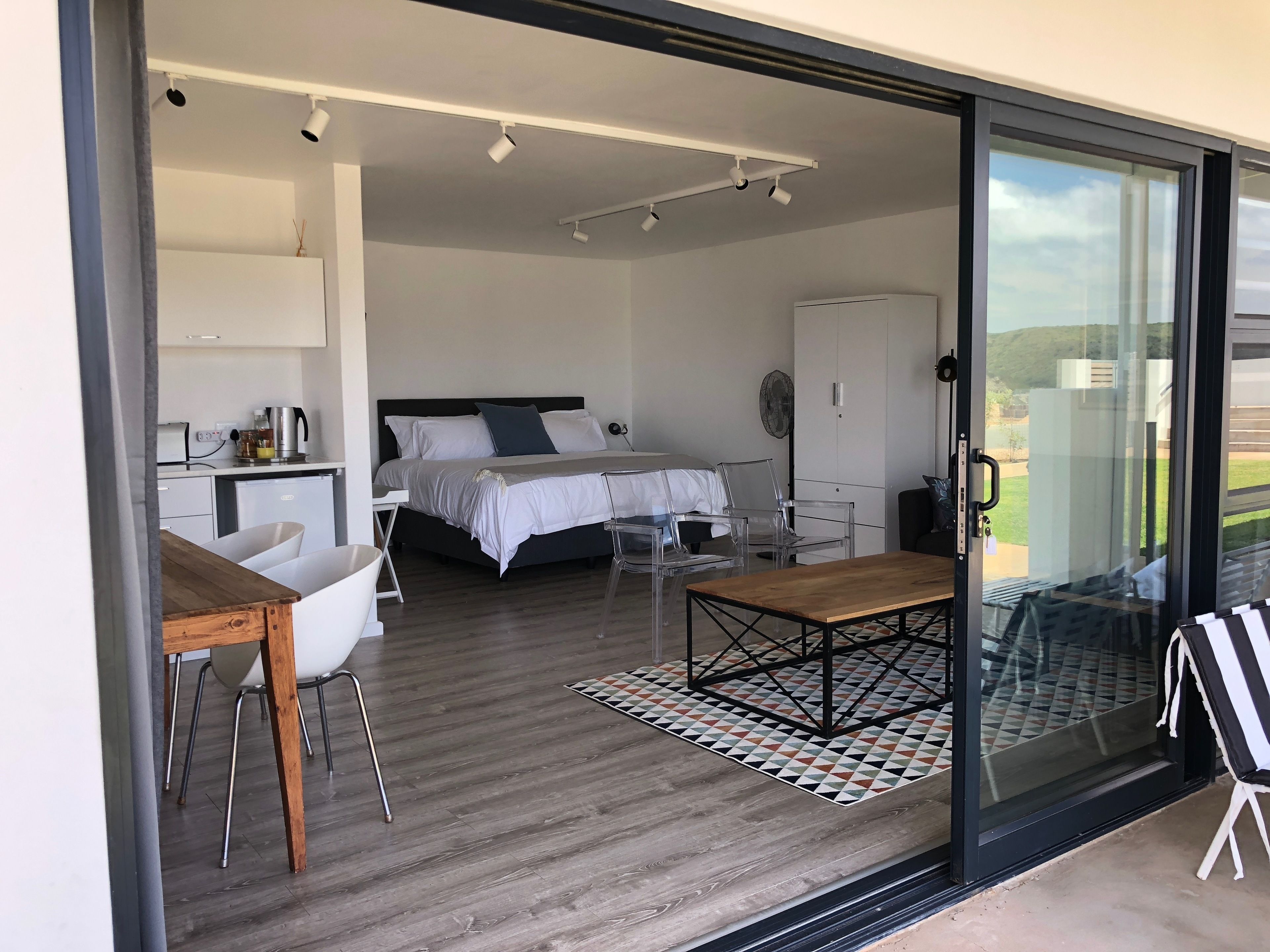 A modern bedroom with a large bed, bedside tables, and a glass door leading to a balcony.