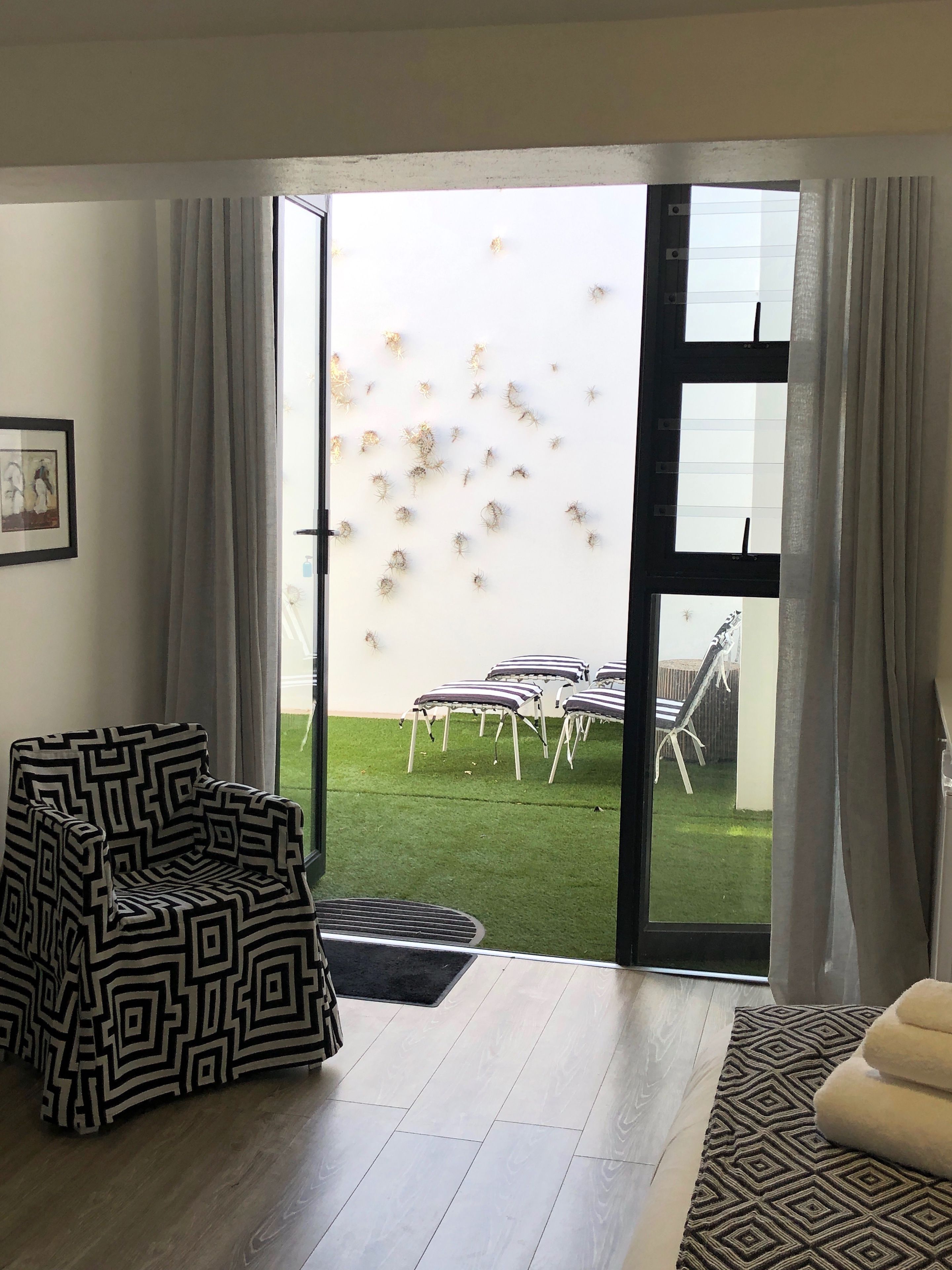 A living room with a patterned armchair, a sofa, and a view of an outdoor area with chairs and a lawn.