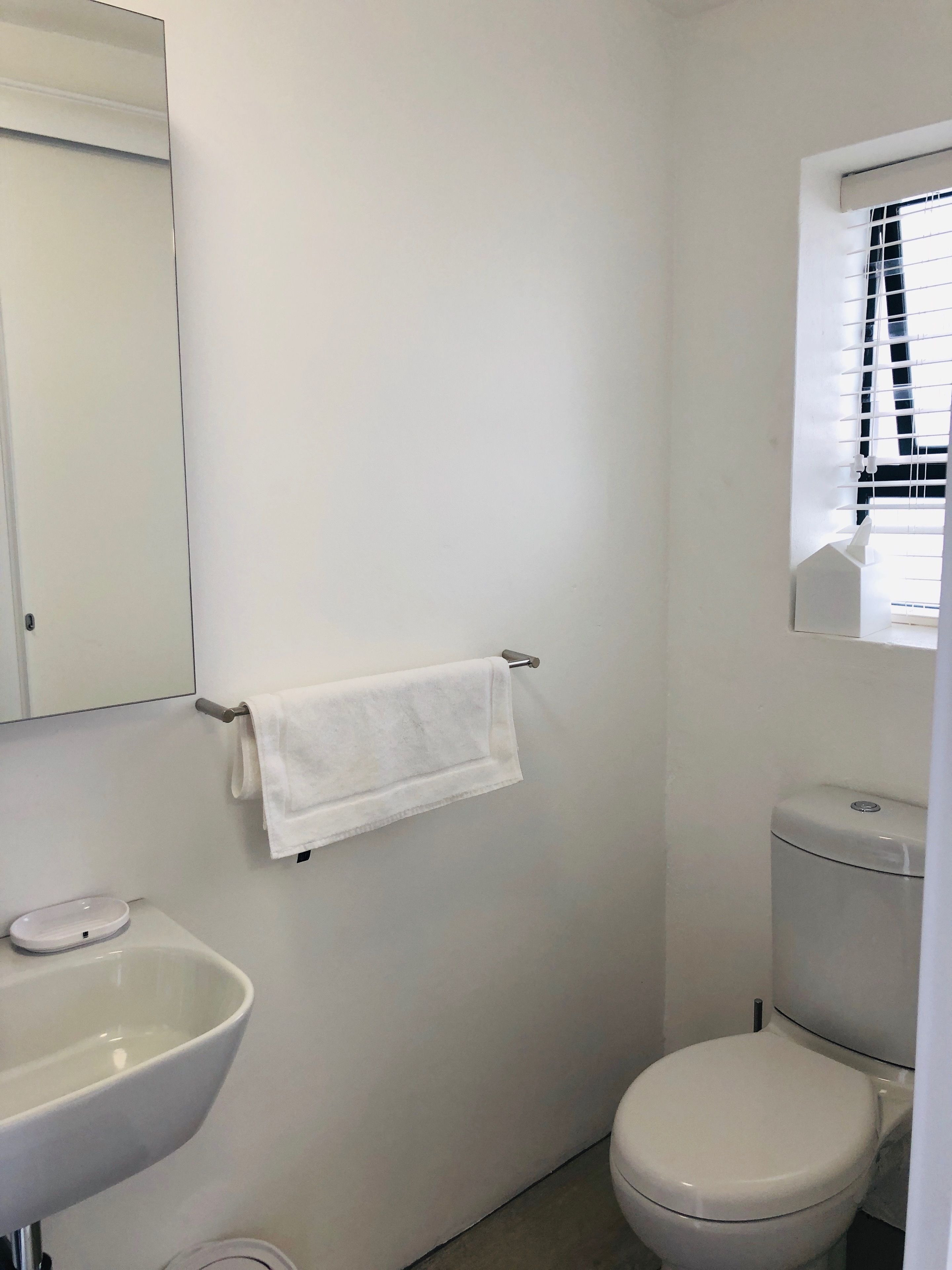 Un baño pequeño y limpio con un lavabo blanco, inodoro y una toalla colgada en un perchero.