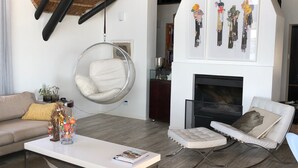 A modern living room with a high ceiling, a fireplace, and a hanging chair. - Karee Manor Guesthouse (Still Bay)