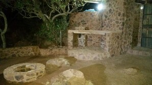 An outdoor stone structure with a bench and a small table, surrounded by stone steps and a tree. - Matalatala (Cullinan)