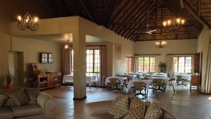A spacious living area with a high ceiling, multiple dining tables, and comfortable seating. - Matalatala (Cullinan)