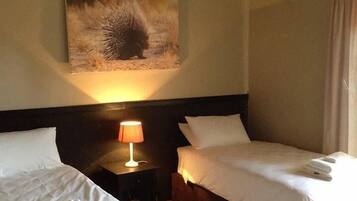 Une chambre d’hôtel avec deux lits, une table de chevet avec une lampe, un tableau au mur et un plafond en chaume.