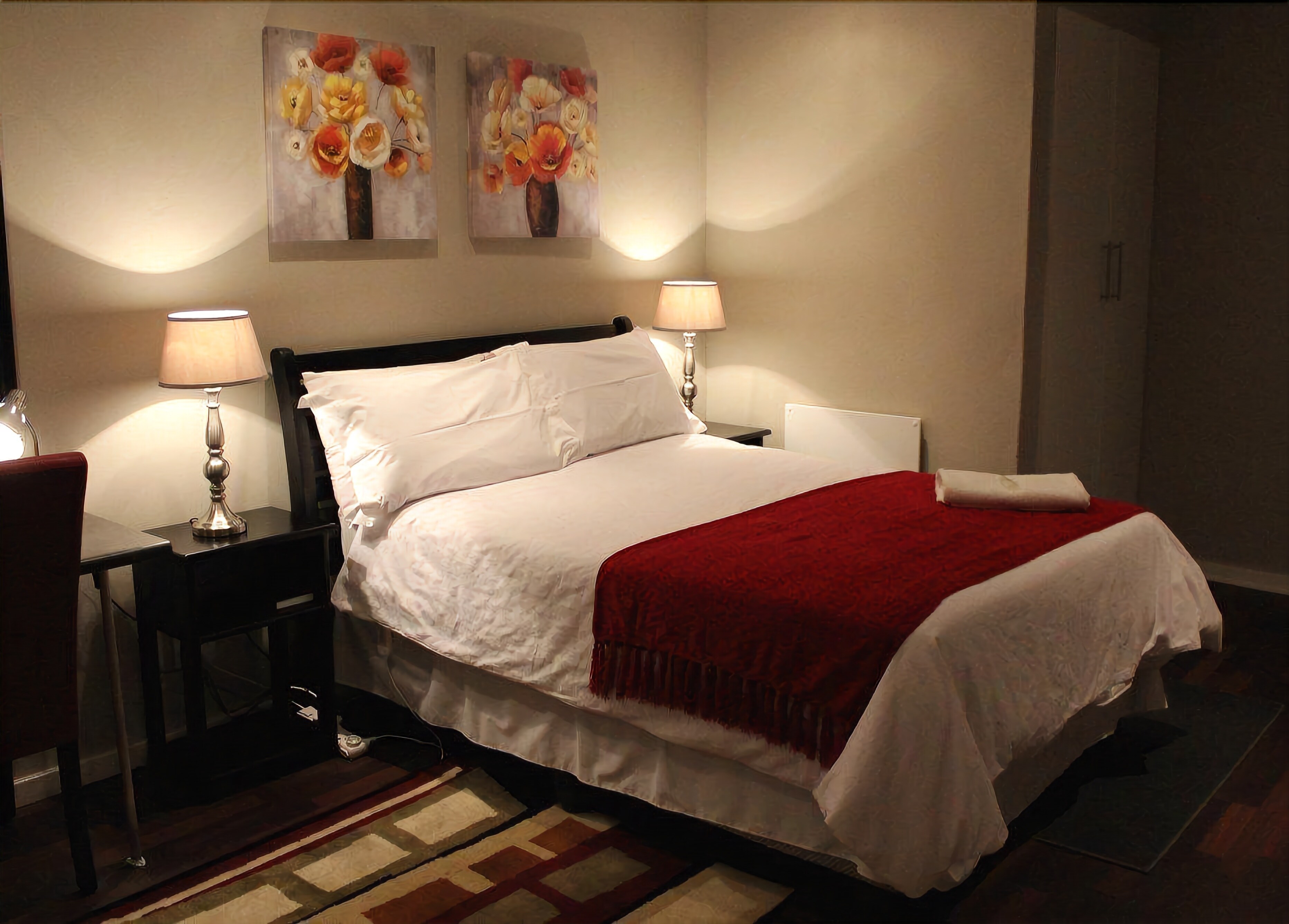 A neatly made bed with white linens and a red throw, flanked by two bedside lamps.