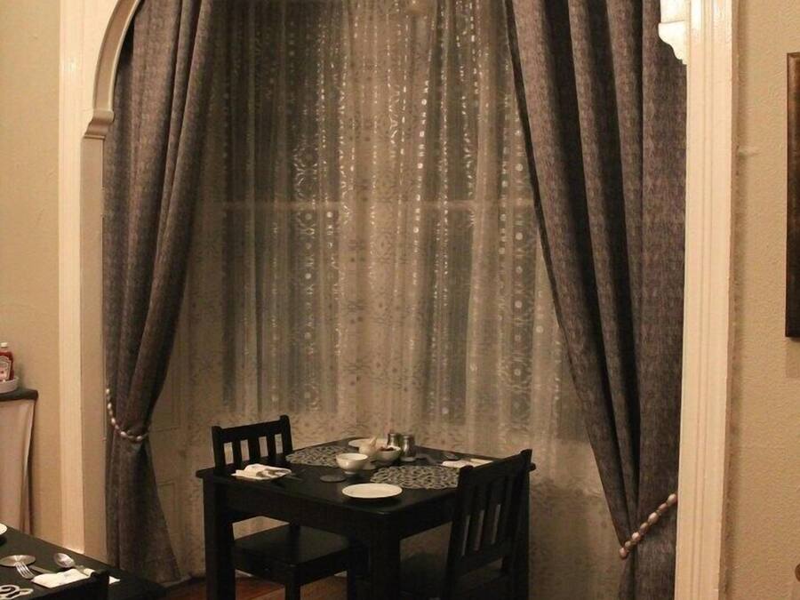 Uma área de refeições com uma mesa posta para dois, cadeiras e uma cortina decorativa.