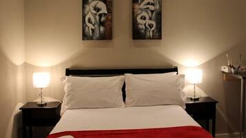 Una habitación de hotel con una cama, dos mesitas de noche, dos lámparas de pared y dos cuadros abstractos.