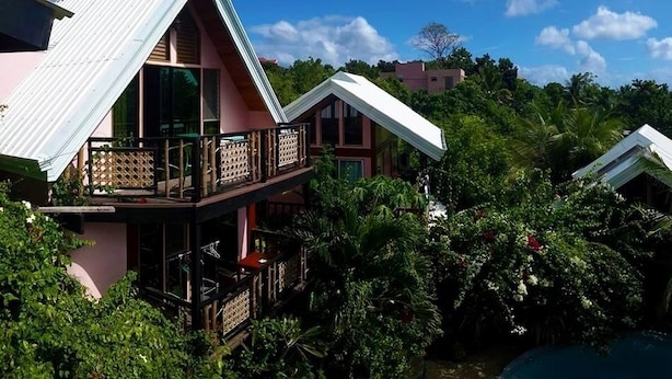 Un edificio de dos pisos con balcón, rodeado de densa vegetación tropical.