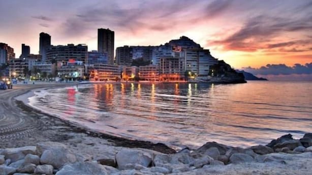 Paisagem costeira urbana ao pôr do sol, com edifícios modernos e mar calmo.