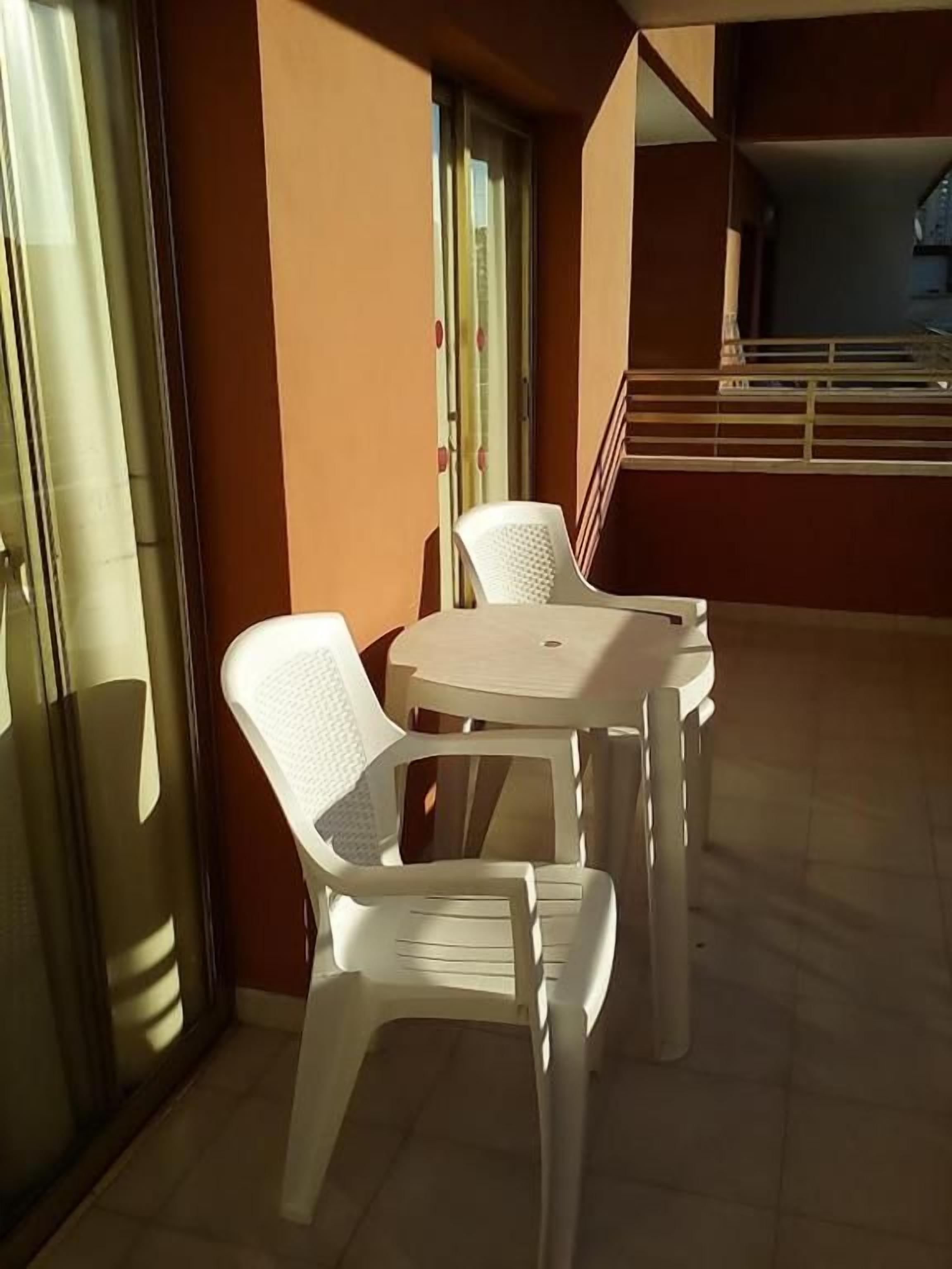 A balcony with a table and two chairs, a staircase in the background, and a glass door.