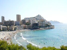 Un paisaje urbano costero con una playa, edificios altos y montañas al fondo.