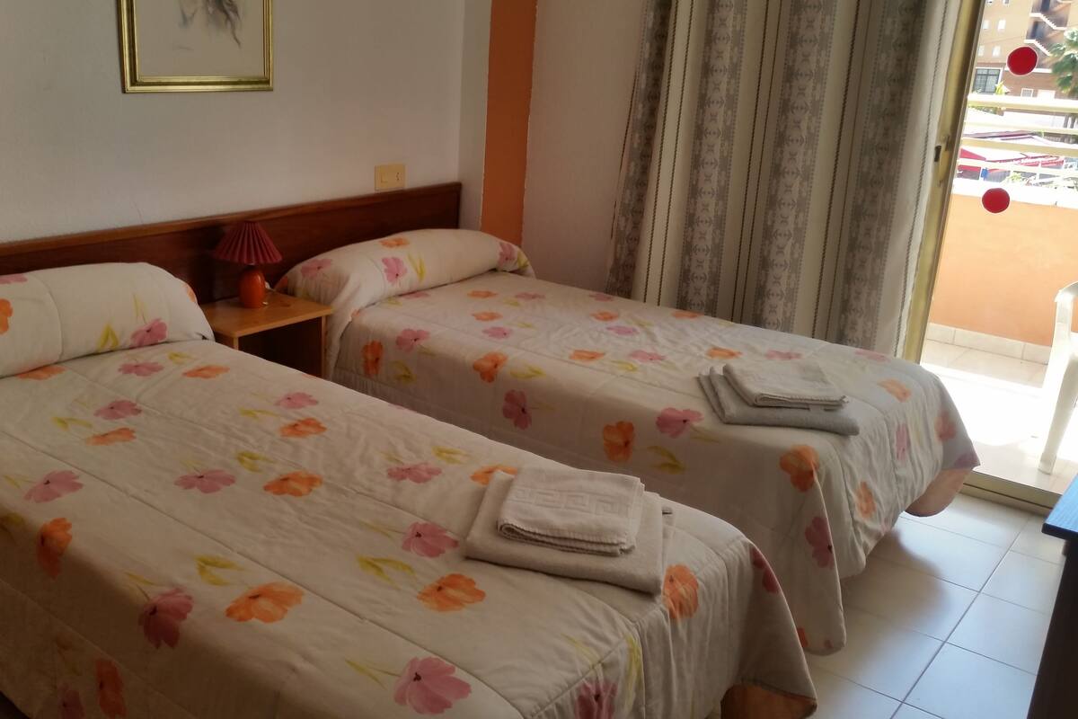 A hotel room with two single beds, each with floral-patterned bedding and a folded towel on the bed.