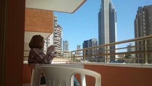 Uma varanda com vista para edifícios altos, uma cadeira de plástico branca e uma pessoa sentada.