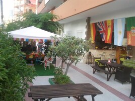 Un espacio de patio al aire libre con mesas y sillas, una carpa blanca y banderas de varios países.