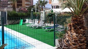 Piscina com área de grama sintética verde, espreguiçadeiras e palmeiras.