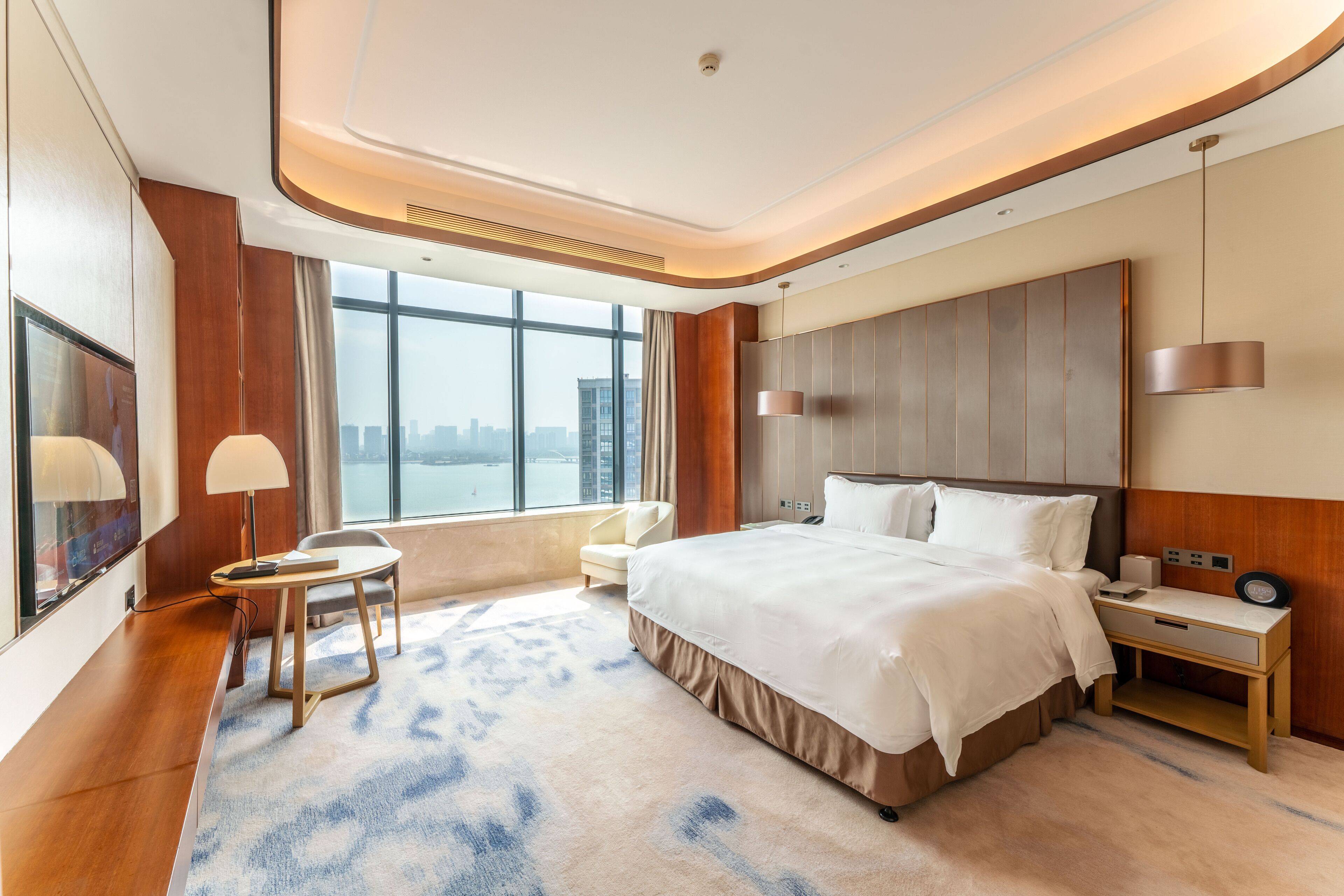 A modern hotel room with a large bed, a desk, a chair, and a view of the city.