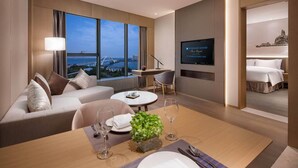 A modern hotel room with a sofa, dining table, TV, and a view of a bridge. - Wyndham Grand Plaza Royale Yuzhou Xiamen (Xiamen)