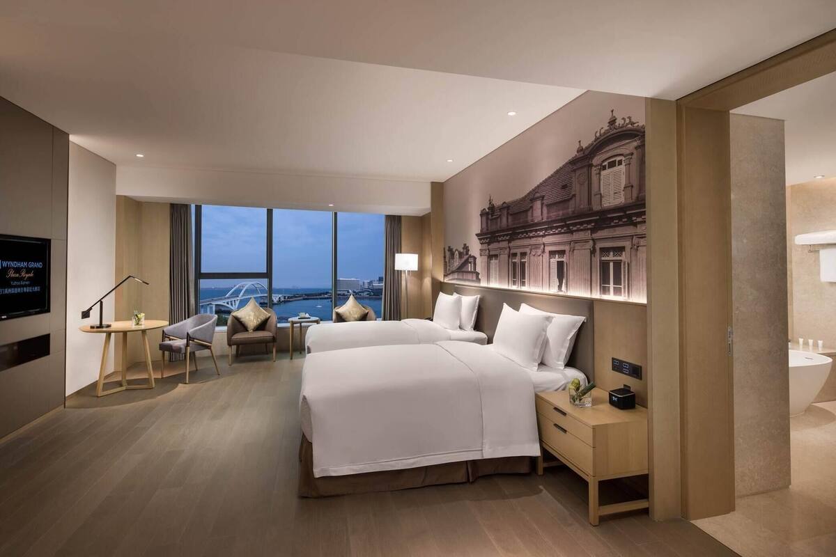 A hotel room with two beds, a TV, a desk, and a view of the cityscape.