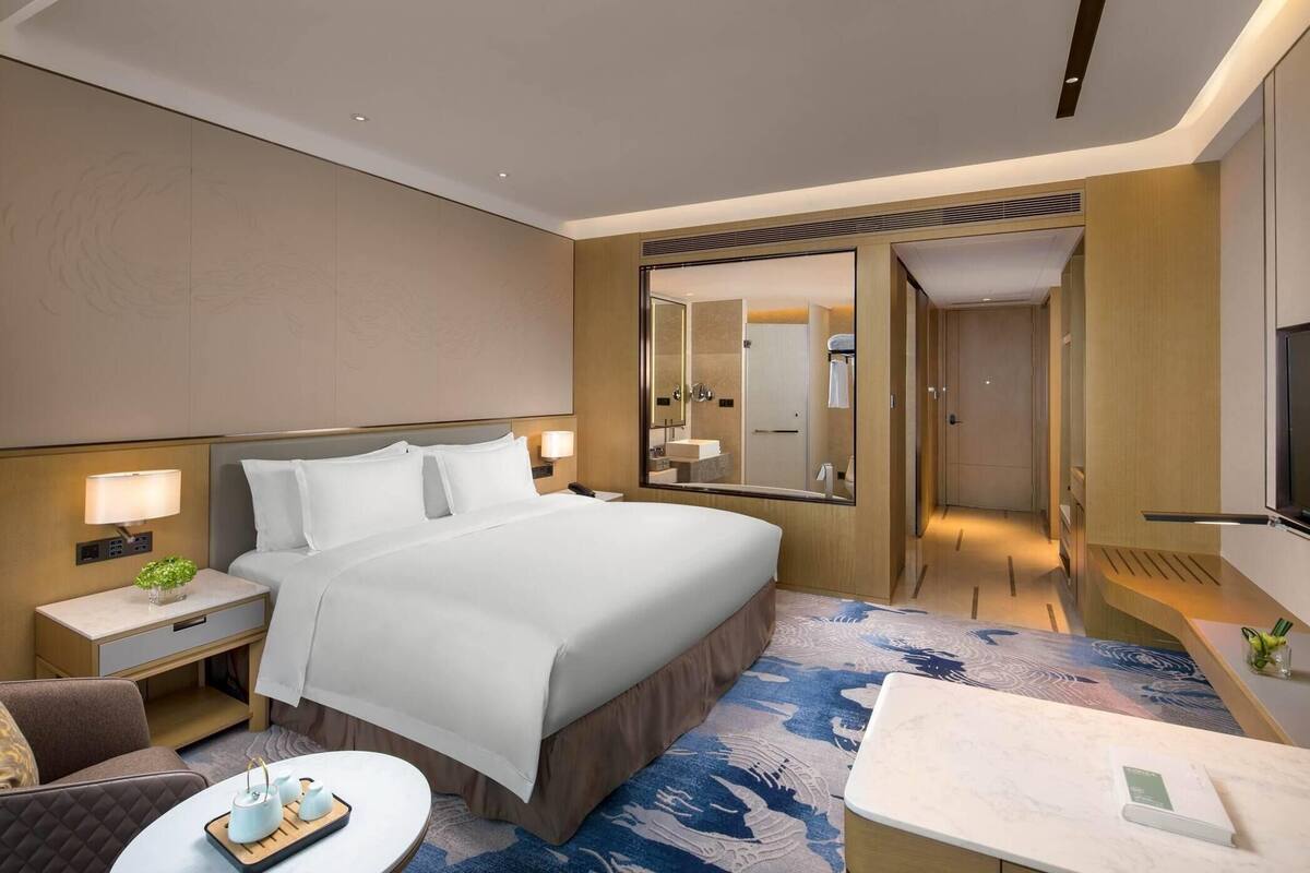 A hotel room with a large bed, bedside tables, a desk, a chair, and a mirror.