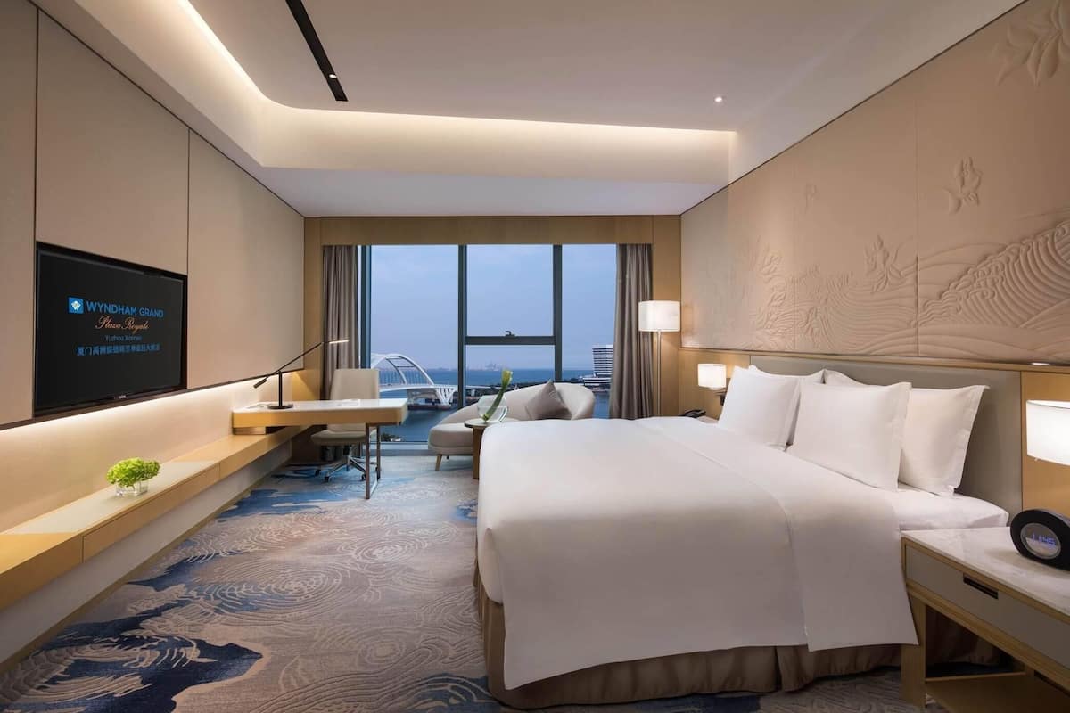 A hotel room with a large bed, a desk with a TV, a chair, and a view of a bridge.