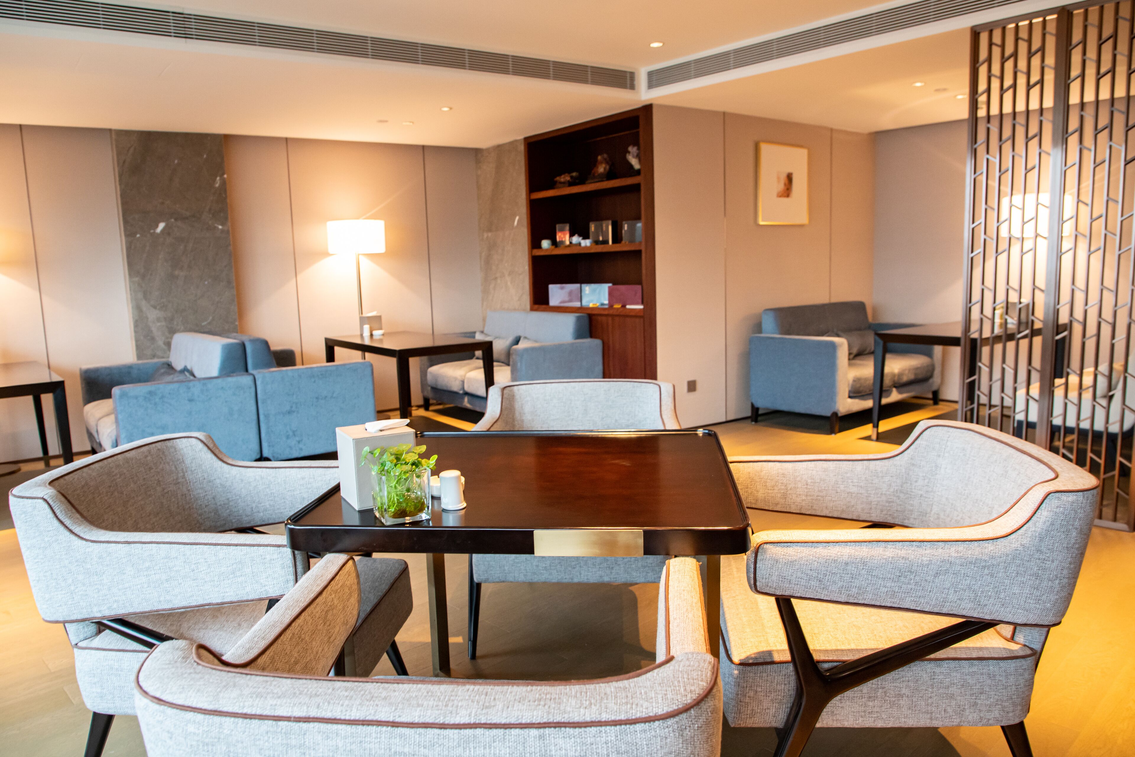 A modern living room with a round table, grey upholstered chairs, a bookshelf, and a floor lamp.