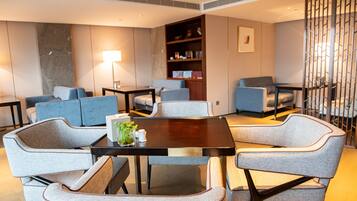 A modern living room with a round table, grey upholstered chairs, a bookshelf, and a floor lamp.