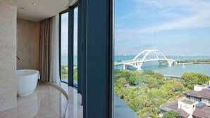 A modern bathroom with a large bathtub, a curved window, and a view of a bridge and greenery. - Wyndham Grand Plaza Royale Yuzhou Xiamen (Xiamen)