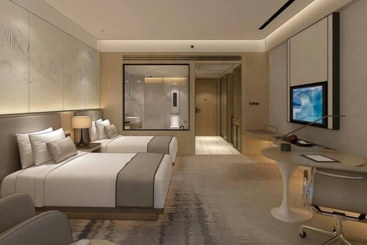 A modern hotel room with a large bed, a desk with a chair, a TV, and a mirror.