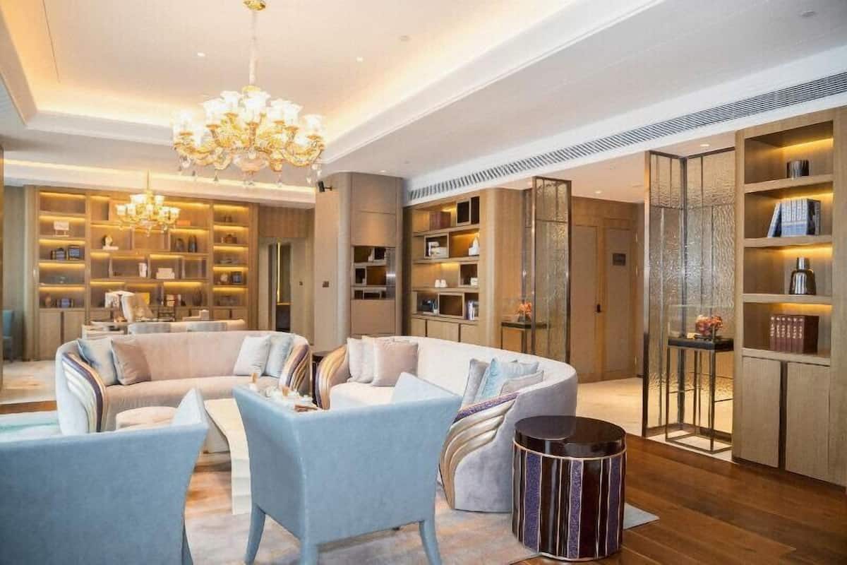 A spacious living area with a large sectional sofa, a round coffee table, and a chandelier. There are built-in bookshelves and a decorative partition with shelves.