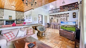 A spacious living room with a high ceiling, a fireplace, a television, and a balcony with bookshelves. - Orange Grove Villa (Nafplio)