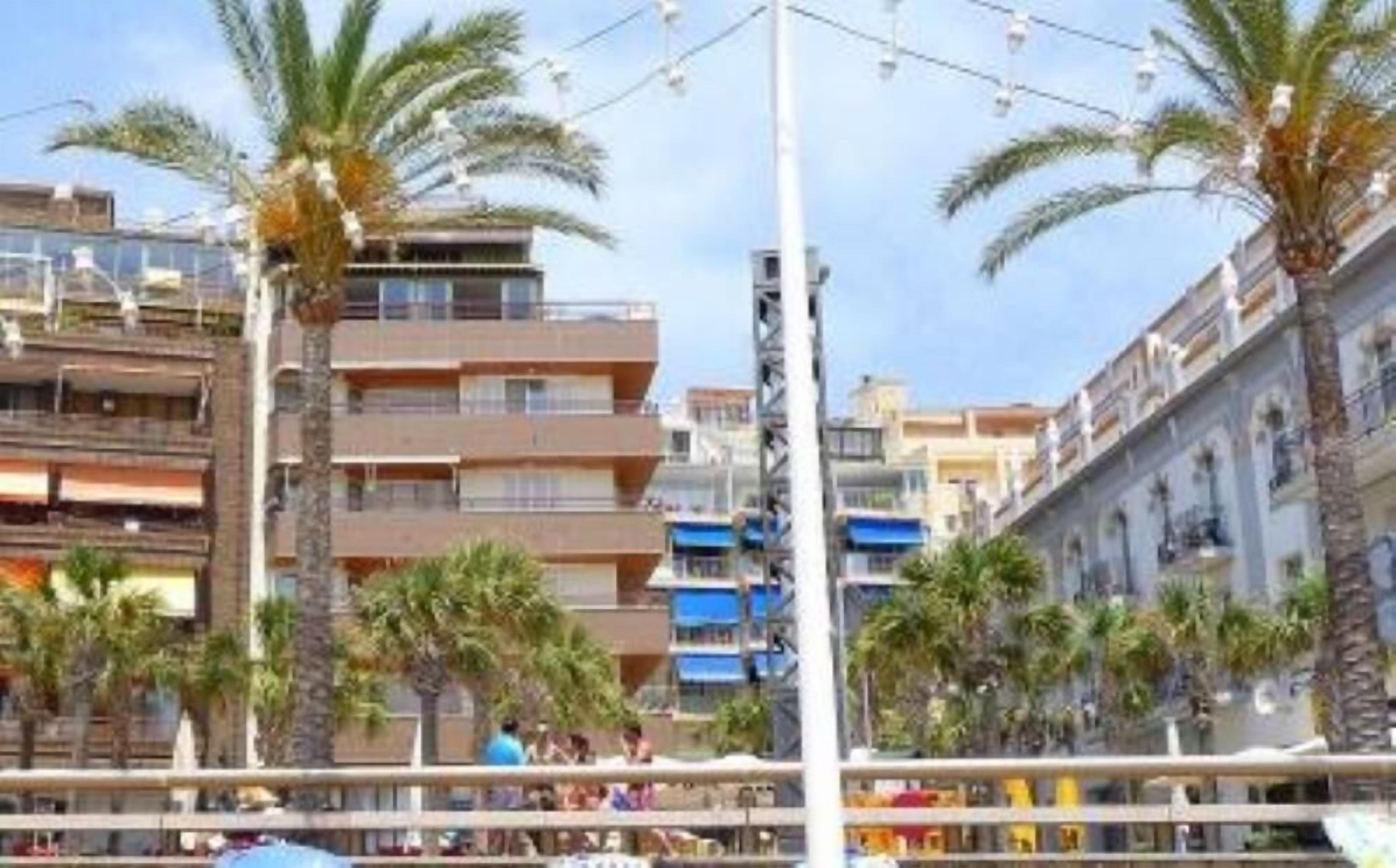 A multi-story building with balconies, palm trees, and a clear sky.