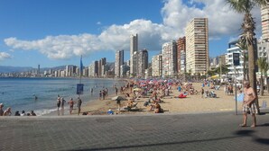 Una spiaggia con una skyline urbana sullo sfondo, caratterizzata da palazzi alti e palme.