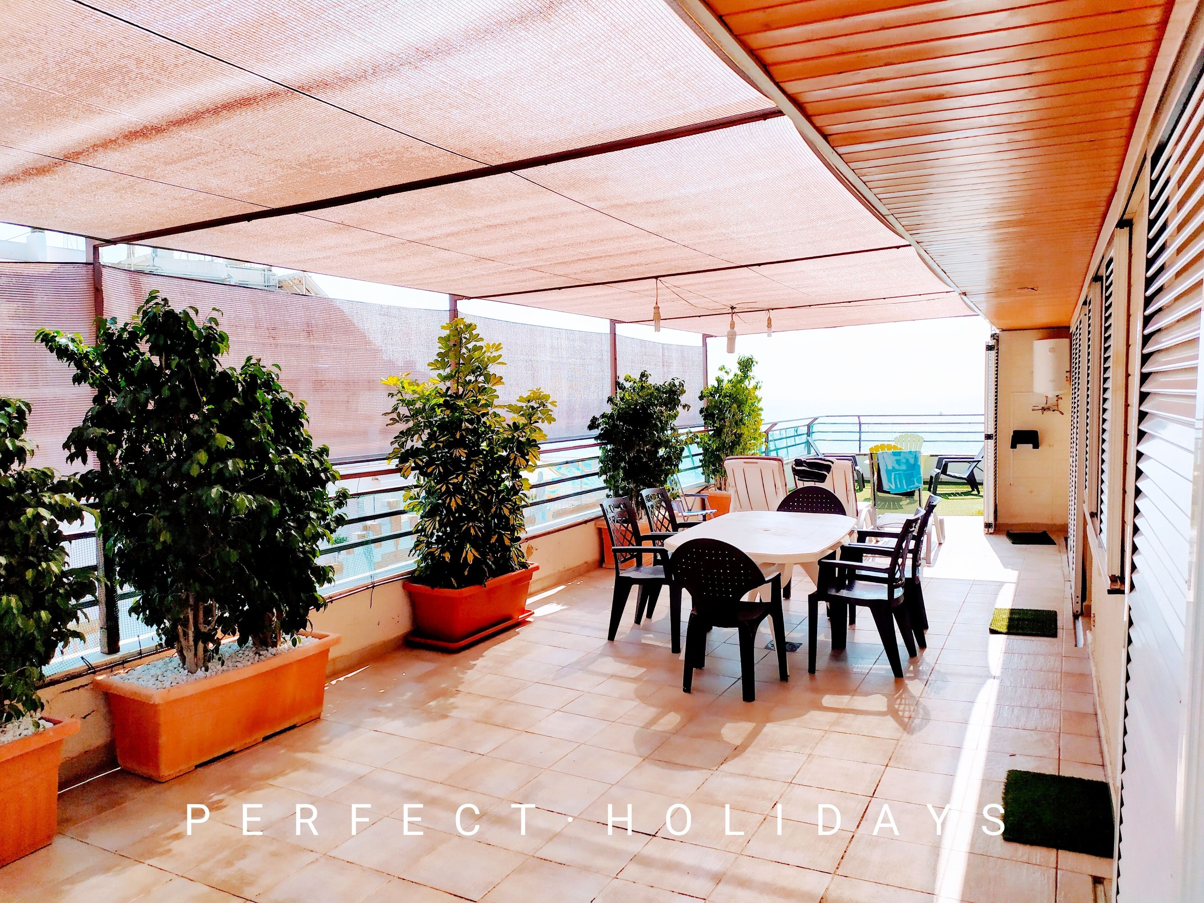 Un espace extérieur aménagé en terrasse, avec une table et des chaises, des plantes en pot et une vue sur la mer.