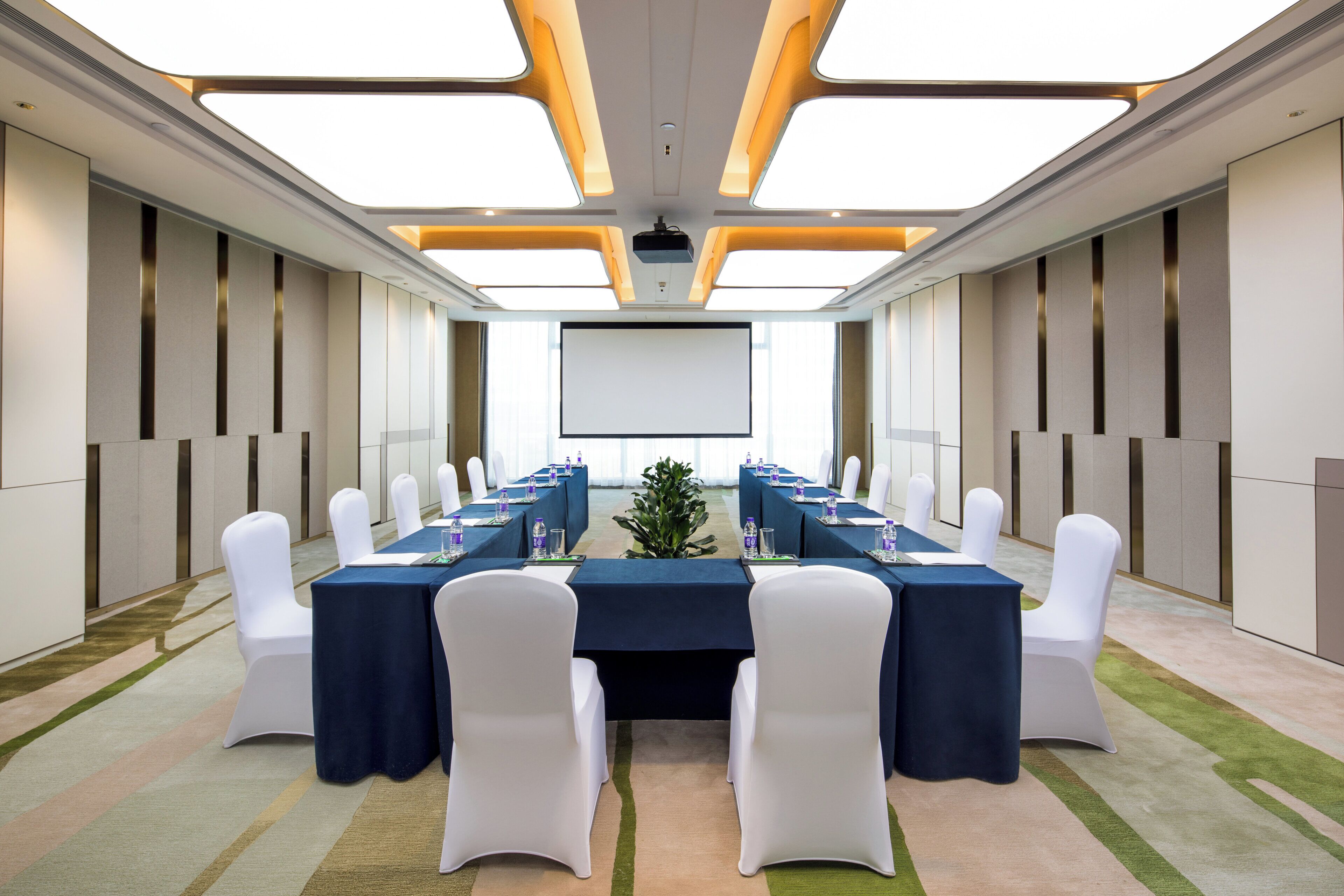 A conference room with a long table, white chairs, and a projector screen at the front.