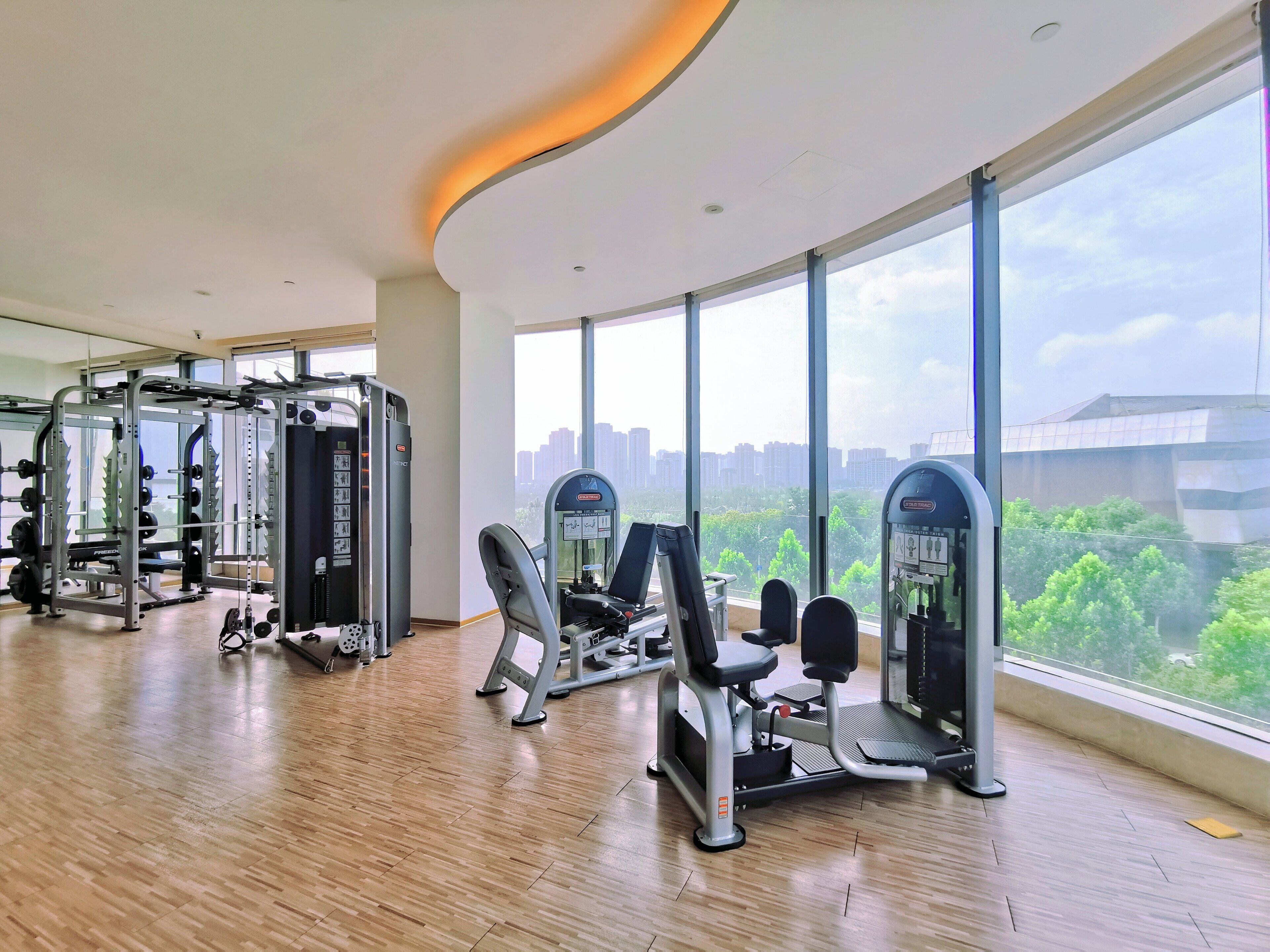 A spacious gym with various exercise equipment and large windows offering a city view.