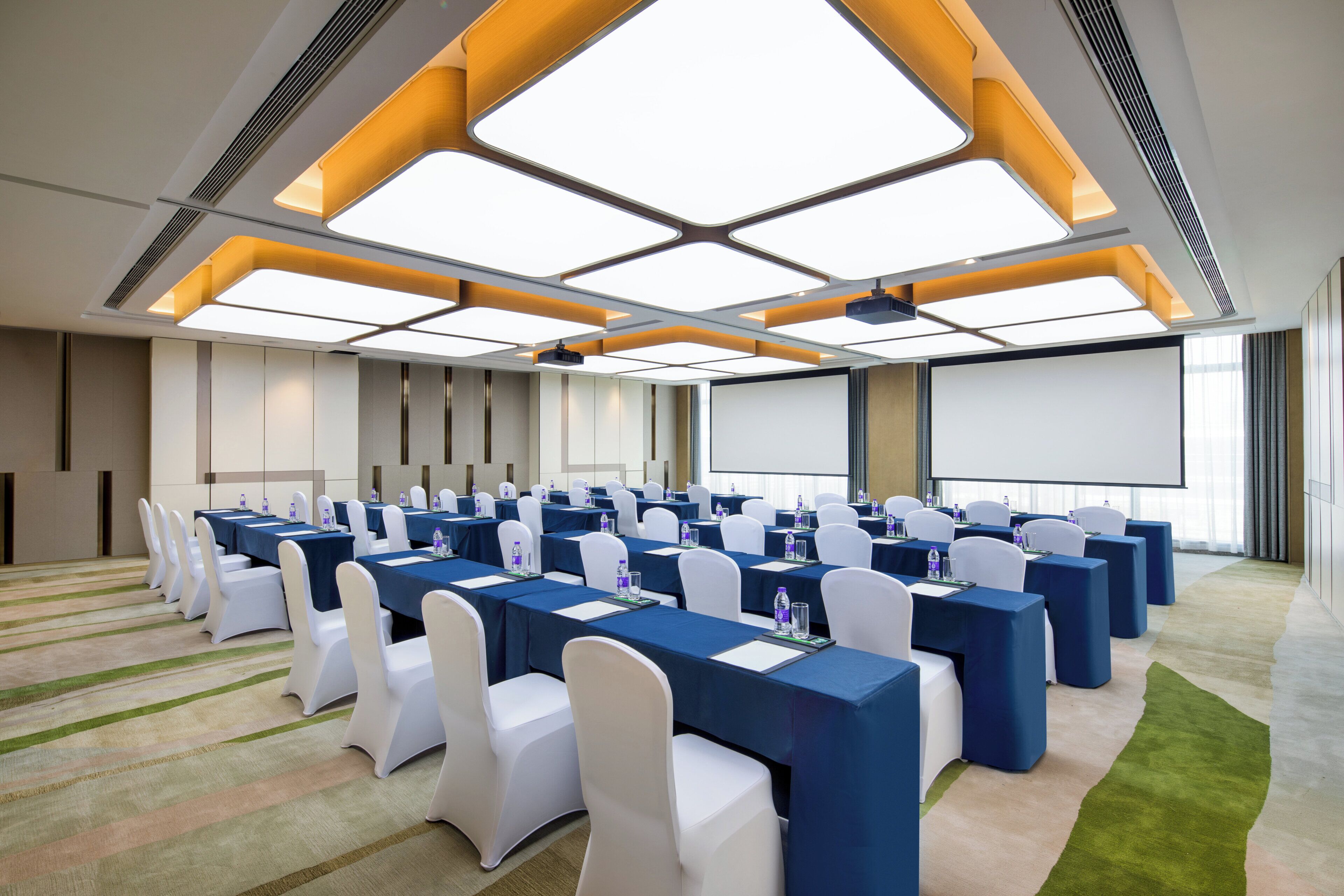 A conference room with multiple tables and chairs, a projector screen, and a large window.