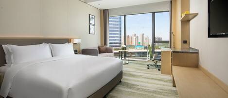 A hotel room with a large bed, a desk, a chair, a TV, and a view of the cityscape.