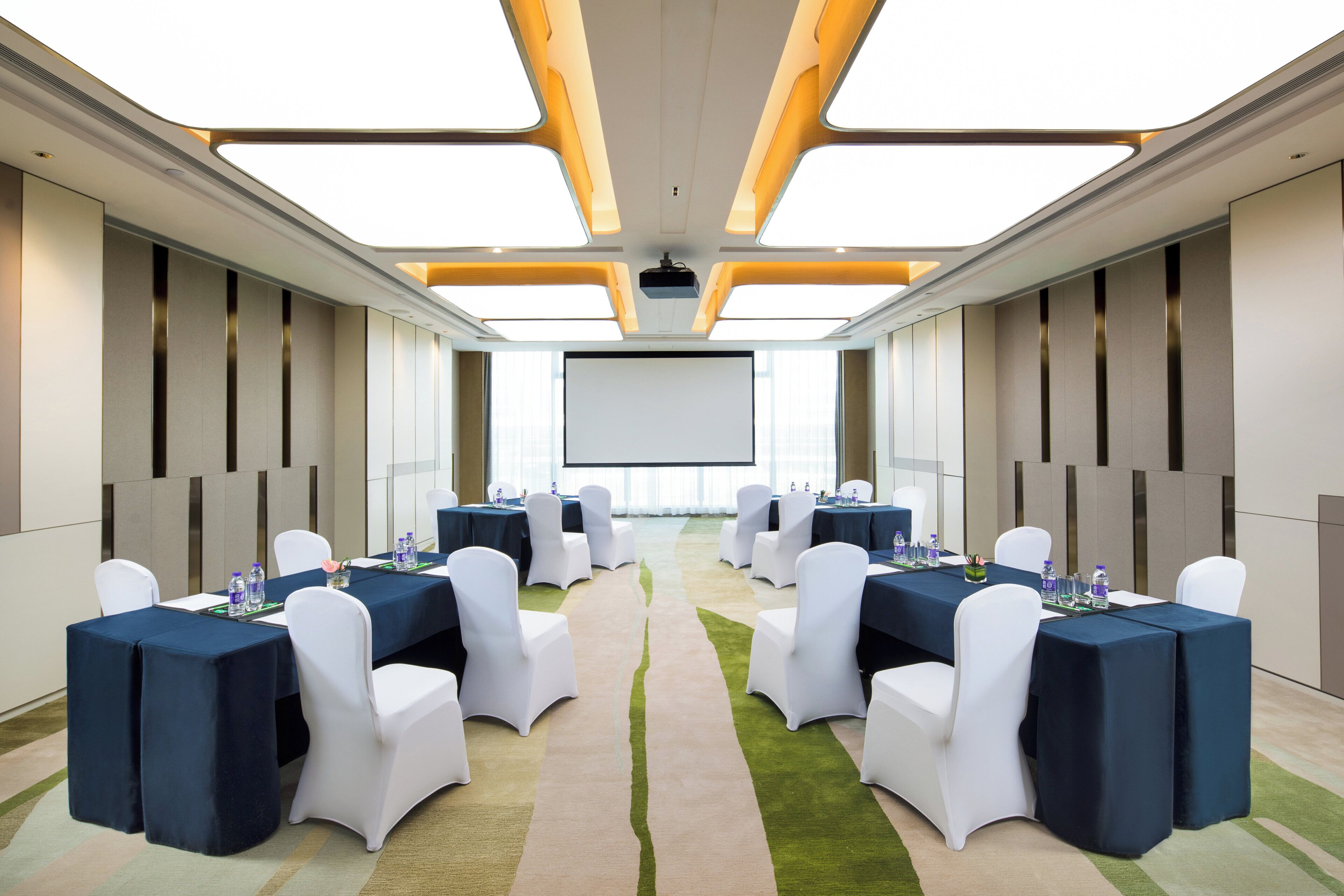 A conference room with tables and chairs, a projector screen, and a large window.