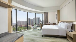 A modern hotel room with a large bed, a desk, and a view of high-rise buildings. - Holiday Inn Zhengzhou Riverside by IHG (Zhengzhou)