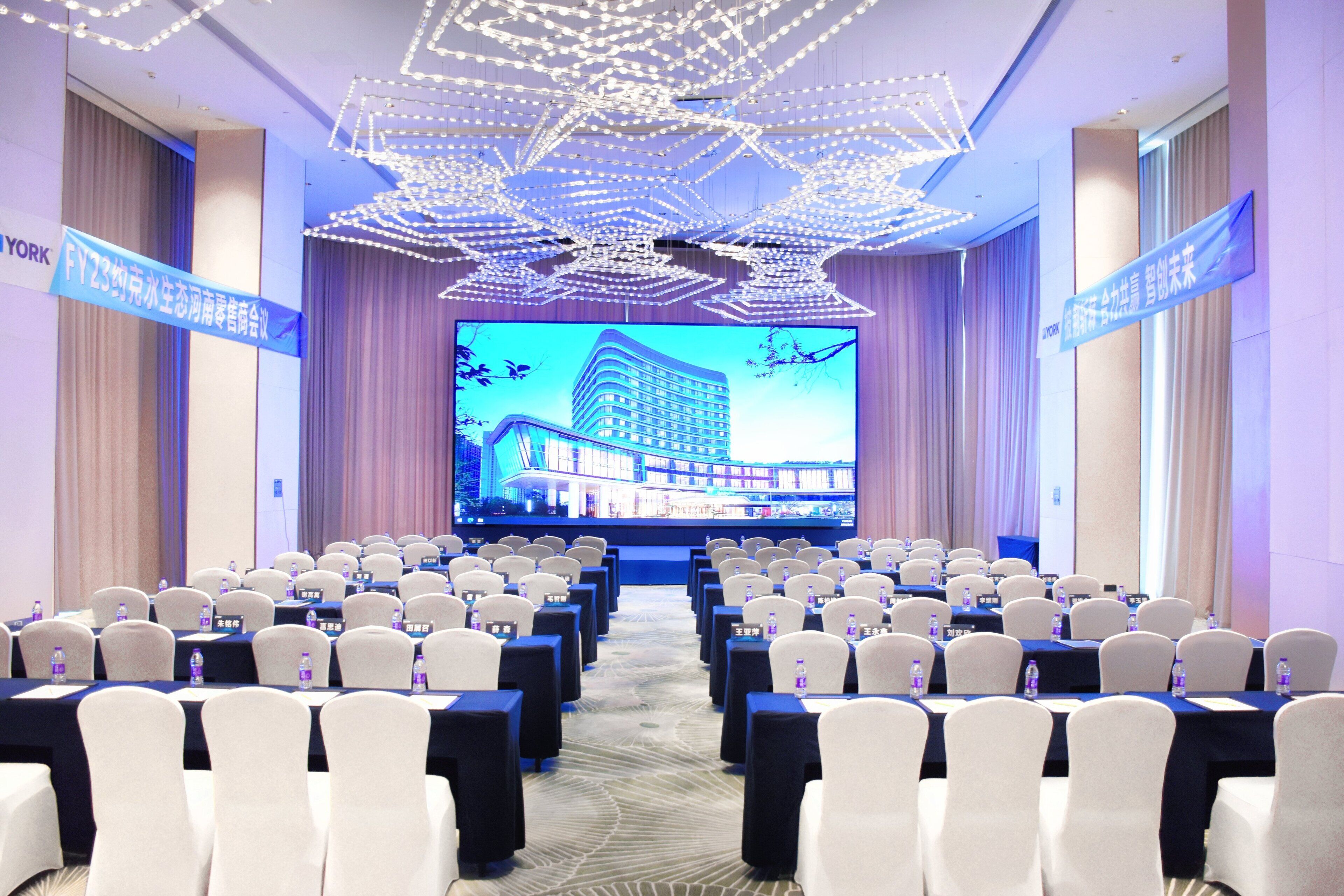 A conference room with rows of chairs, a large screen displaying a building, and banners on the walls.