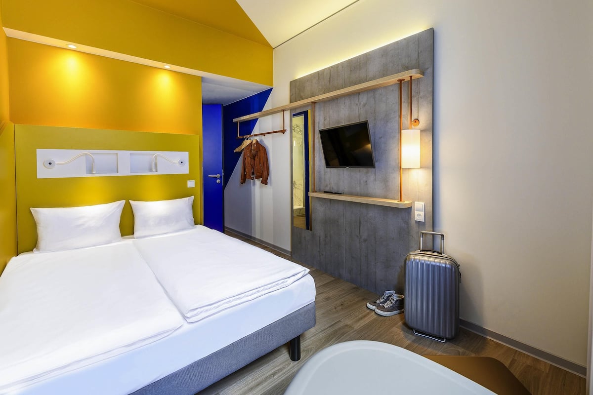 Une chambre d’hôtel avec un lit, une télévision, un miroir et une valise.