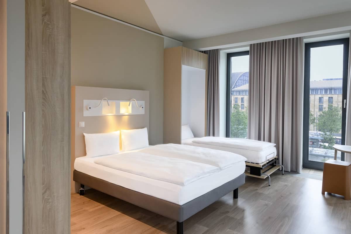Une chambre d’hôtel moderne avec deux lits, une grande fenêtre avec des rideaux et une vue sur la ville.