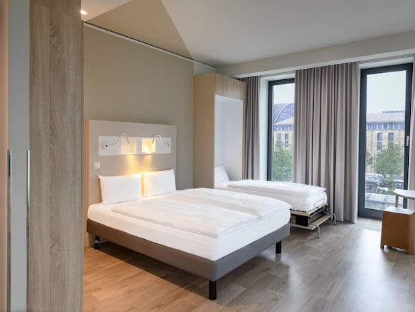 Una habitación de hotel moderna con dos camas, un ventanal con cortinas y vistas a la ciudad.