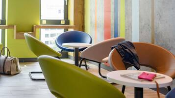 Un interior moderno con sillas de colores, una mesita redonda y una pared de hormigón con rayas verticales.